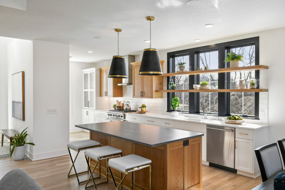 This is an example of a large transitional galley eat-in kitchen in Minneapolis with a drop-in sink, recessed-panel cabinets, light wood cabinets, quartz benchtops, white splashback, ceramic splashback, stainless steel appliances, light hardwood floors, with island, brown floor and white benchtop.