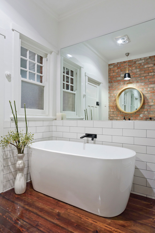 Mid-sized contemporary 3/4 bathroom in Melbourne with flat-panel cabinets, light wood cabinets, a freestanding tub, a wall-mount toilet, white tile, porcelain tile, white walls, painted wood floors, an integrated sink and engineered quartz benchtops.