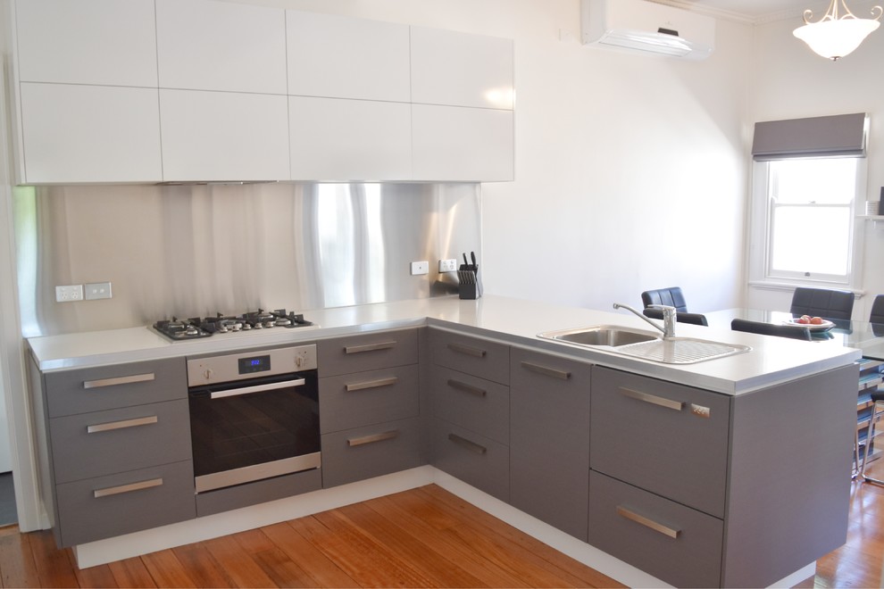 Small modern l-shaped eat-in kitchen in Sydney with a single-bowl sink, flat-panel cabinets, grey cabinets, laminate benchtops, metallic splashback, stainless steel appliances, a peninsula, metal splashback and medium hardwood floors.