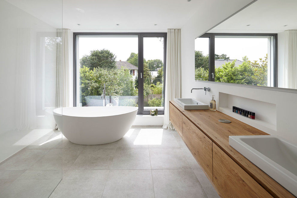 Inspiration for a contemporary 3/4 bathroom in Cologne with flat-panel cabinets, light wood cabinets, a freestanding tub, limestone, a vessel sink, wood benchtops, an open shower, white tile, white walls, white floor, a curbless shower and brown benchtops.