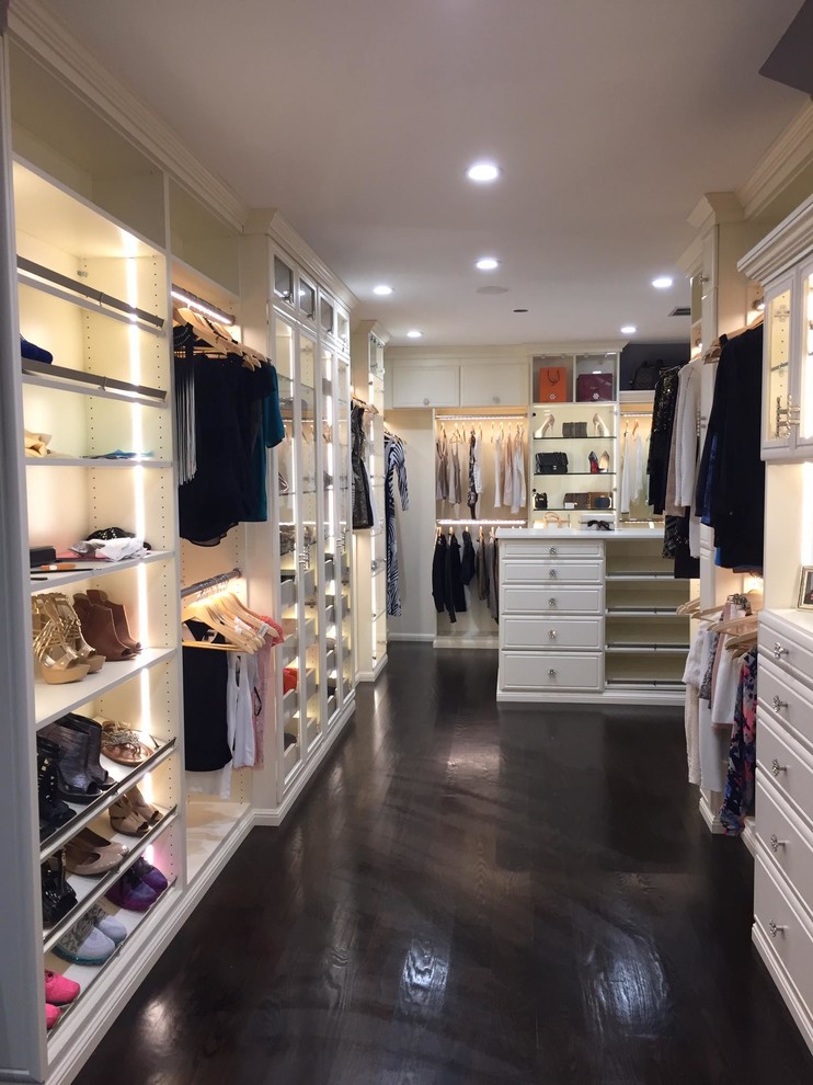 This is an example of a large midcentury women's walk-in wardrobe in Los Angeles with glass-front cabinets, dark hardwood floors, black floor and beige cabinets.