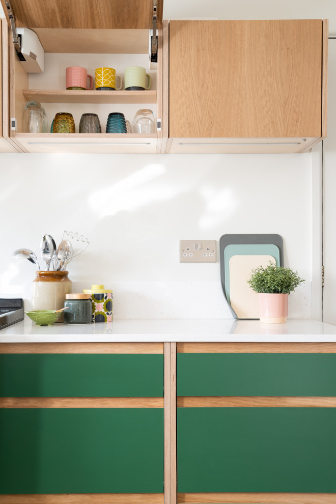 Mid-sized midcentury u-shaped eat-in kitchen in West Midlands with an integrated sink, flat-panel cabinets, green cabinets, solid surface benchtops, white splashback, glass tile splashback, coloured appliances, vinyl floors, with island, multi-coloured floor and white benchtop.