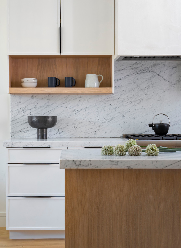 This is an example of a large contemporary open plan kitchen in San Francisco with white cabinets, marble worktops, white splashback, marble splashback, stainless steel appliances, light hardwood flooring, an island and white worktops.