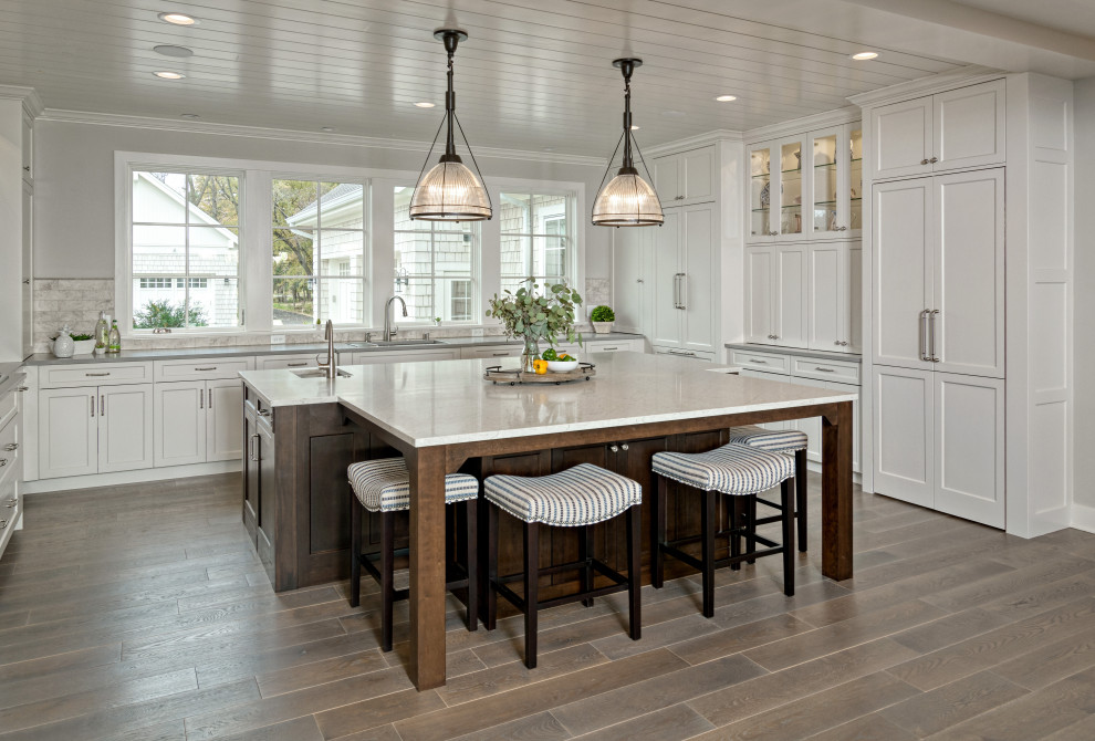 This is an example of an expansive beach style u-shaped kitchen in Minneapolis with an undermount sink, white cabinets, granite benchtops, stone tile splashback, laminate floors, with island, brown floor, grey benchtop, shaker cabinets, grey splashback and timber.