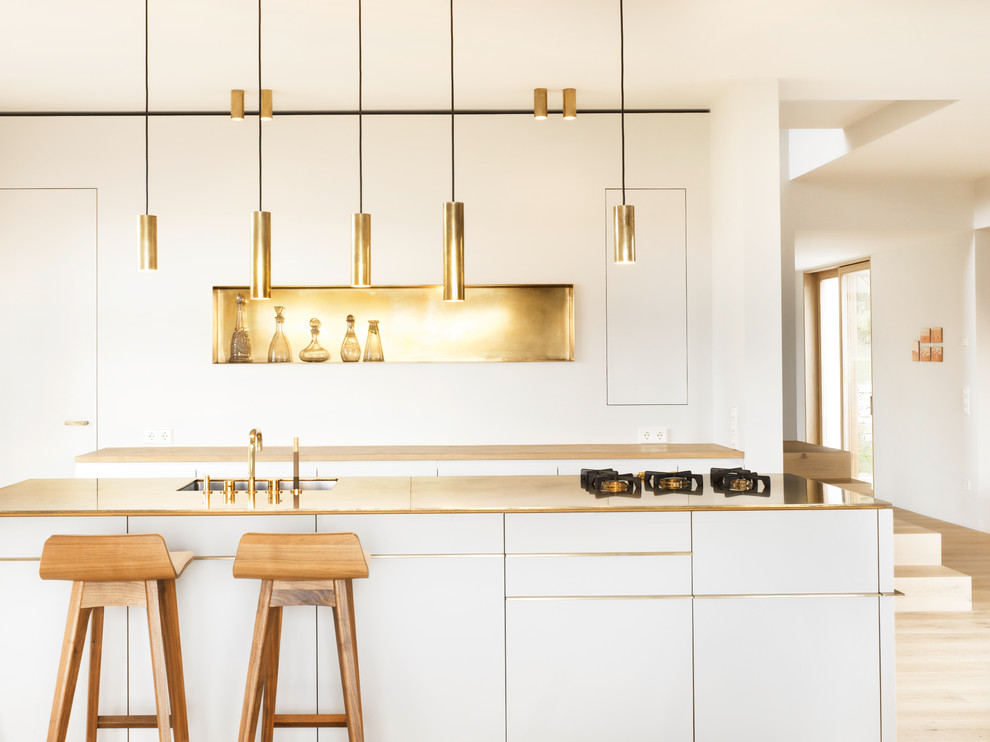 Scandinavian kitchen in Munich with an undermount sink, flat-panel cabinets, white cabinets, white splashback, panelled appliances, light hardwood floors and with island.