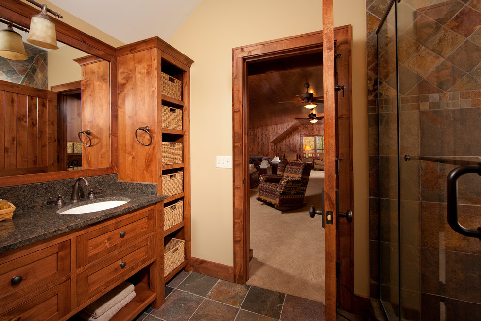 Small country 3/4 bathroom in Minneapolis with an undermount sink, recessed-panel cabinets, medium wood cabinets, granite benchtops, an alcove shower, a two-piece toilet, brown tile, stone tile, beige walls and slate floors.