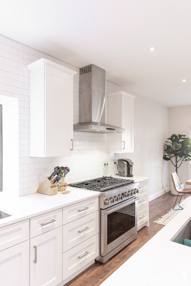 Inspiration for a mid-sized transitional eat-in kitchen in Phoenix with shaker cabinets, white cabinets, white splashback, subway tile splashback, stainless steel appliances, medium hardwood floors, with island and brown floor.