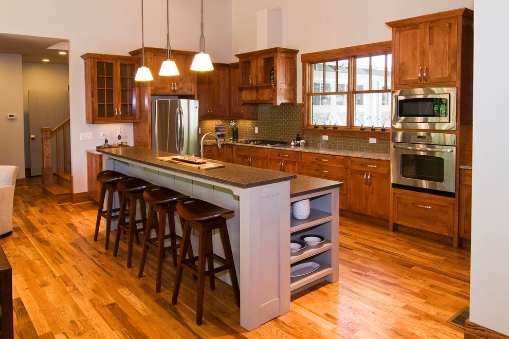 Mid-sized arts and crafts galley medium tone wood floor open concept kitchen photo with an undermount sink, shaker cabinets, medium tone wood cabinets, granite countertops, gray backsplash, ceramic backsplash, stainless steel appliances and an island