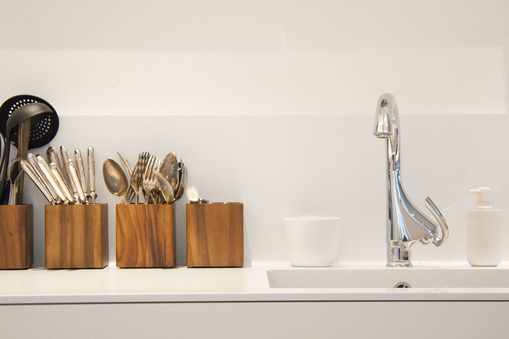 Cette image montre cuisine in U With un évier intégré, un placard à porte affleurante, des portes de placard blanches, un plan de travail en surface solide, une crédence blanche, parquet clair, îlot, un sol beige and un plan de travail blanc.