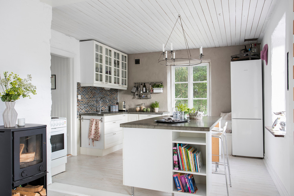 This is an example of a mid-sized country l-shaped open plan kitchen in Malmo with glass-front cabinets, white cabinets, light hardwood floors, with island, concrete benchtops, brown splashback and matchstick tile splashback.