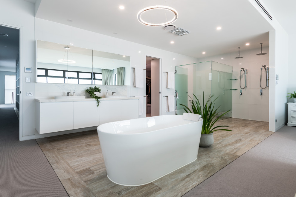 This is an example of a large contemporary master bathroom in Gold Coast - Tweed with flat-panel cabinets, white cabinets, a freestanding tub, a double shower, a one-piece toilet, white tile, porcelain tile, white walls, wood-look tile, a drop-in sink, engineered quartz benchtops, multi-coloured floor, an open shower, white benchtops, an enclosed toilet, a double vanity and a floating vanity.