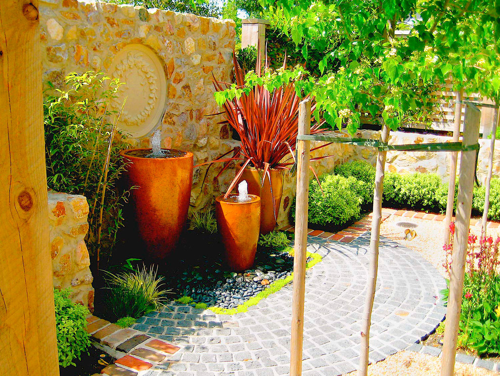This is an example of a small mediterranean courtyard patio in Sacramento with a water feature, natural stone pavers and a pergola.