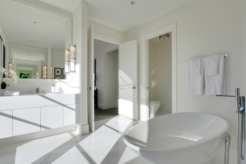 Inspiration for a mid-sized contemporary master bathroom in Calgary with flat-panel cabinets, white cabinets, a freestanding tub, white walls, porcelain floors, an undermount sink, engineered quartz benchtops, white floor and white benchtops.