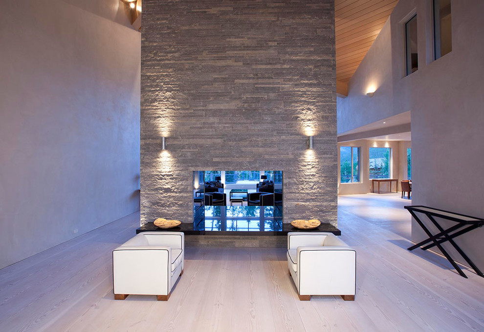 This is an example of a contemporary open concept living room in Denver with white walls, light hardwood floors, a two-sided fireplace and a stone fireplace surround.