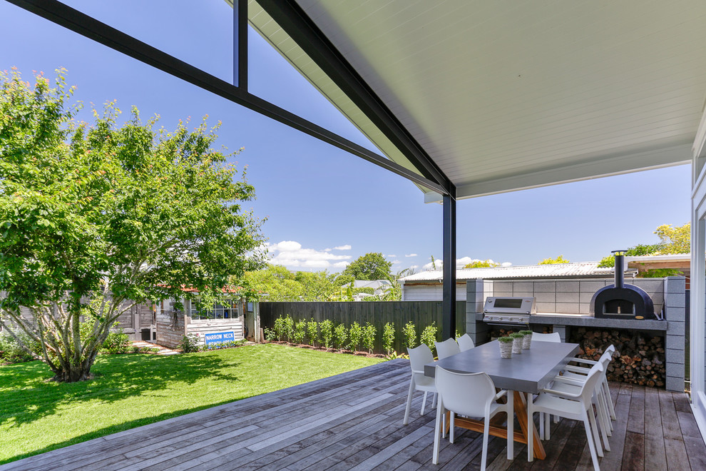 This is an example of a large transitional backyard deck in Auckland with with fireplace and a roof extension.