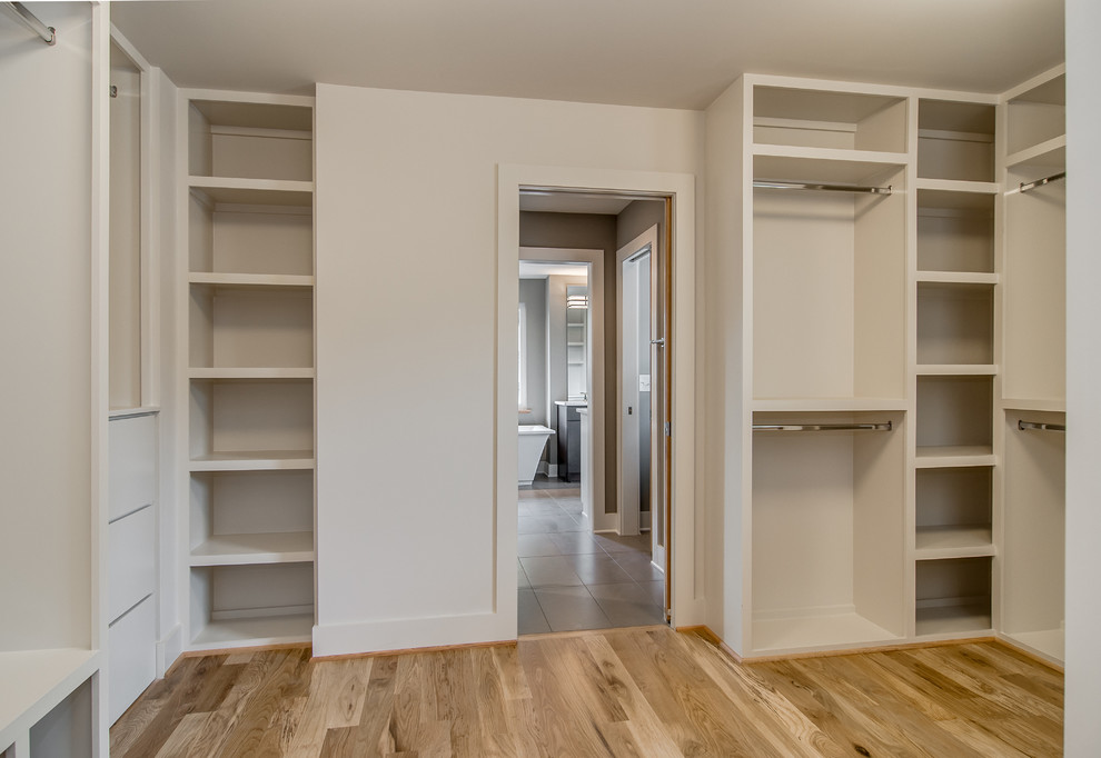 Inspiration for a large modern gender-neutral walk-in wardrobe in Nashville with open cabinets, white cabinets and light hardwood floors.
