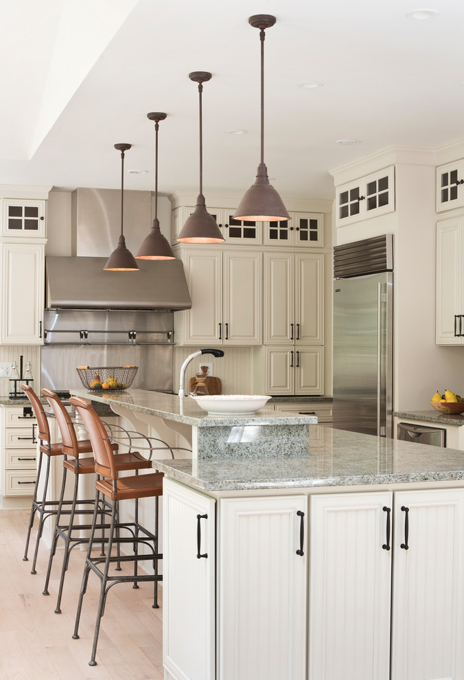 This is an example of a large traditional kitchen in New York with raised-panel cabinets, beige cabinets, metallic splashback, stainless steel appliances, with island, beige floor, grey benchtop, granite benchtops and metal splashback.