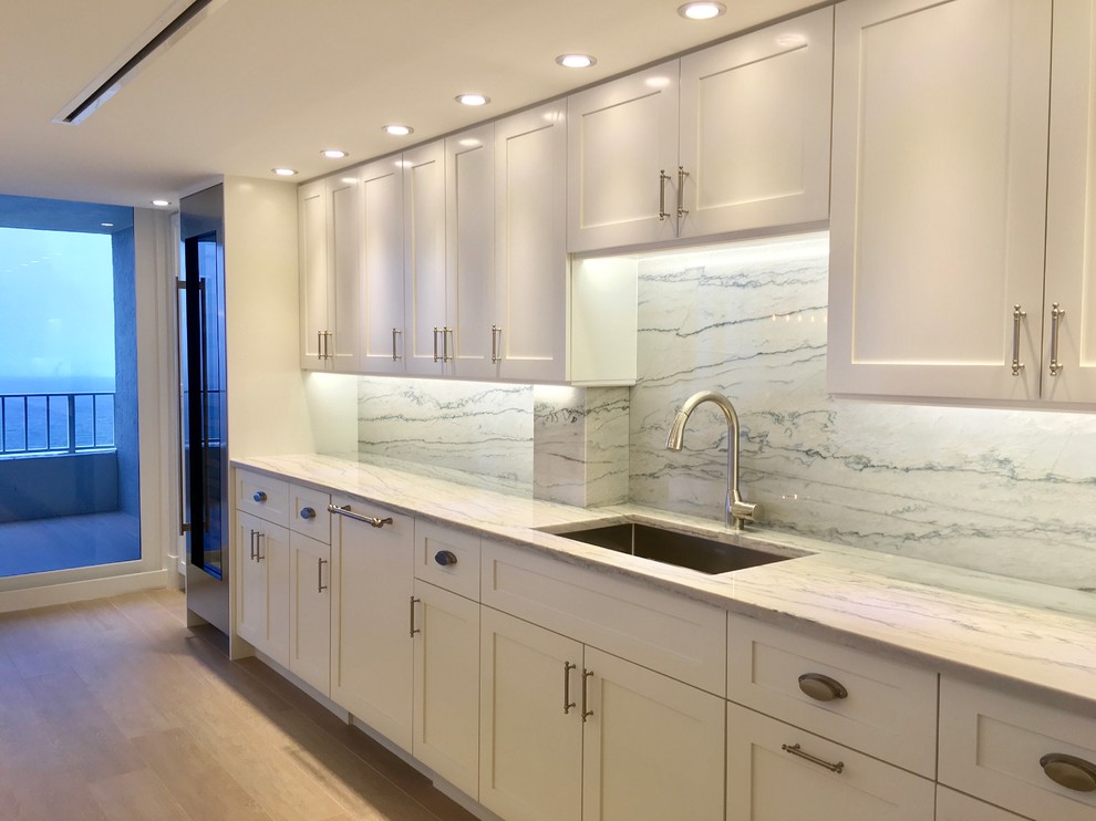 Inspiration for a large transitional galley light wood floor and beige floor open concept kitchen remodel in Miami with an undermount sink, shaker cabinets, white cabinets, marble countertops, gray backsplash, marble backsplash, stainless steel appliances and an island