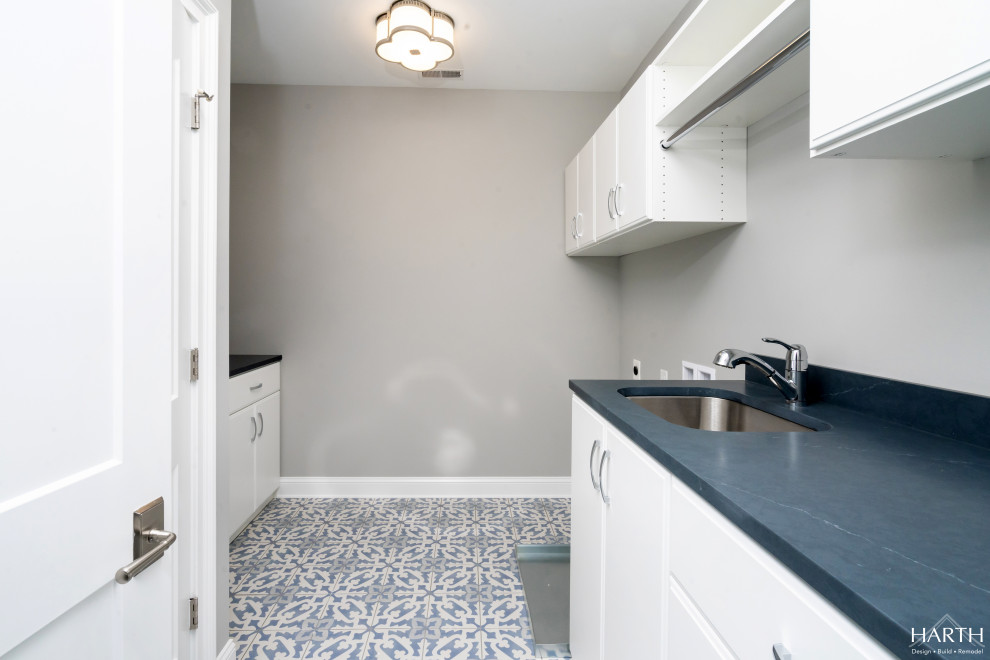 Inspiration for a mid-sized galley dedicated laundry room in Philadelphia with an undermount sink, flat-panel cabinets, white cabinets, soapstone benchtops, black splashback, engineered quartz splashback, grey walls, porcelain floors, a side-by-side washer and dryer, multi-coloured floor and black benchtop.