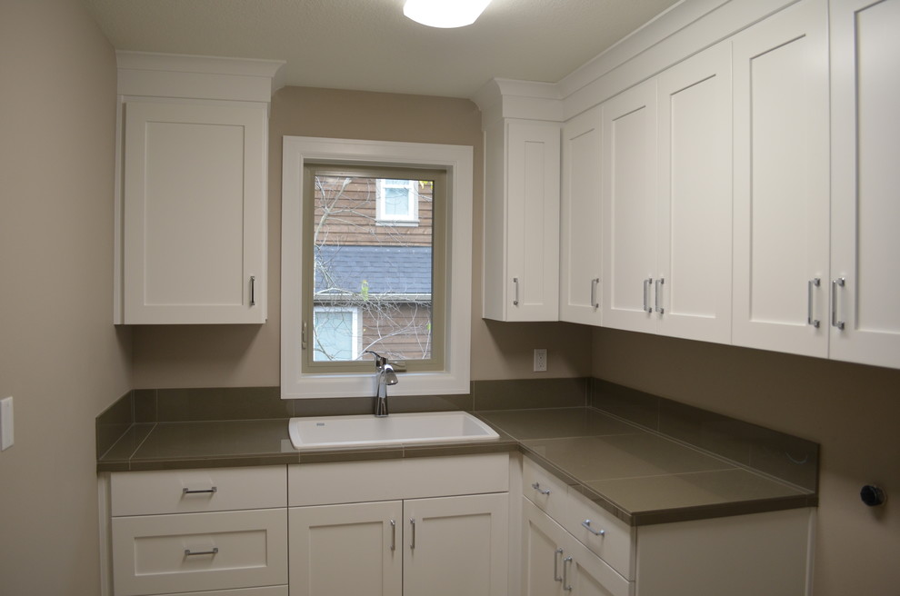Design ideas for a large traditional l-shaped dedicated laundry room in Portland with a drop-in sink, shaker cabinets, white cabinets, tile benchtops, grey walls, travertine floors and a side-by-side washer and dryer.