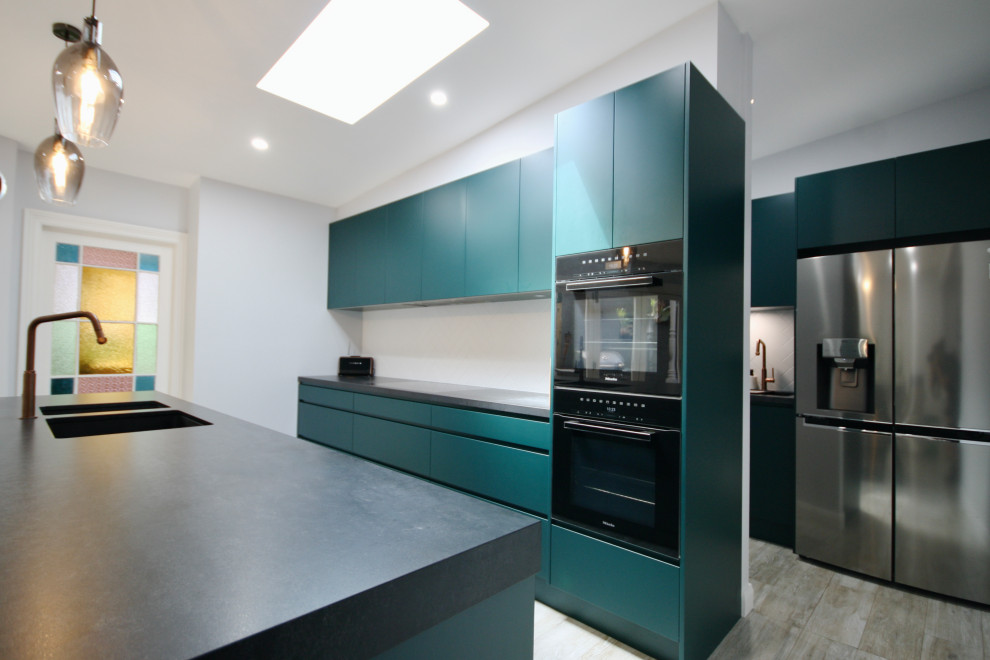 Large industrial open plan kitchen in Sydney with an undermount sink, flat-panel cabinets, green cabinets, quartz benchtops, white splashback, subway tile splashback, black appliances, medium hardwood floors, with island, brown floor, black benchtop and coffered.
