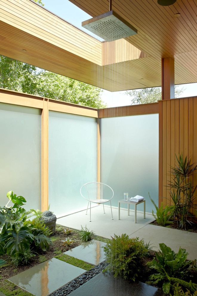 Photo of a midcentury patio with an outdoor shower, concrete slab and a roof extension.