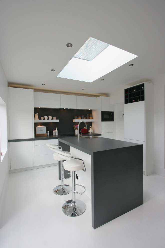 Inspiration for a medium sized modern kitchen/diner in London with a built-in sink, flat-panel cabinets, white cabinets, laminate countertops, black appliances, white walls, an island, painted wood flooring and black splashback.