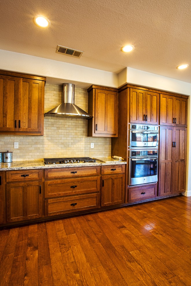 Inspiration for a large rustic dark wood floor and brown floor open concept kitchen remodel in Sacramento with a farmhouse sink, shaker cabinets, brown cabinets, granite countertops, beige backsplash, subway tile backsplash, stainless steel appliances, an island and brown countertops
