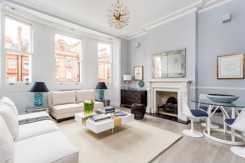 This is an example of a transitional living room in London with blue walls, light hardwood floors, a standard fireplace and grey floor.