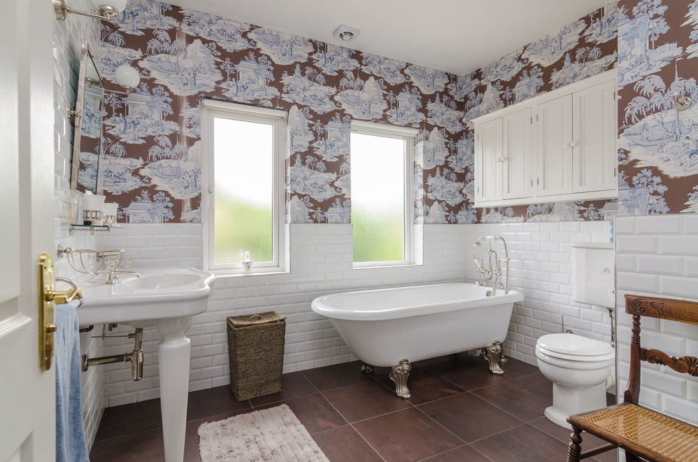 Photo of a traditional master bathroom in Belfast with a claw-foot tub, a two-piece toilet, white tile, subway tile, multi-coloured walls, a console sink and brown floor.