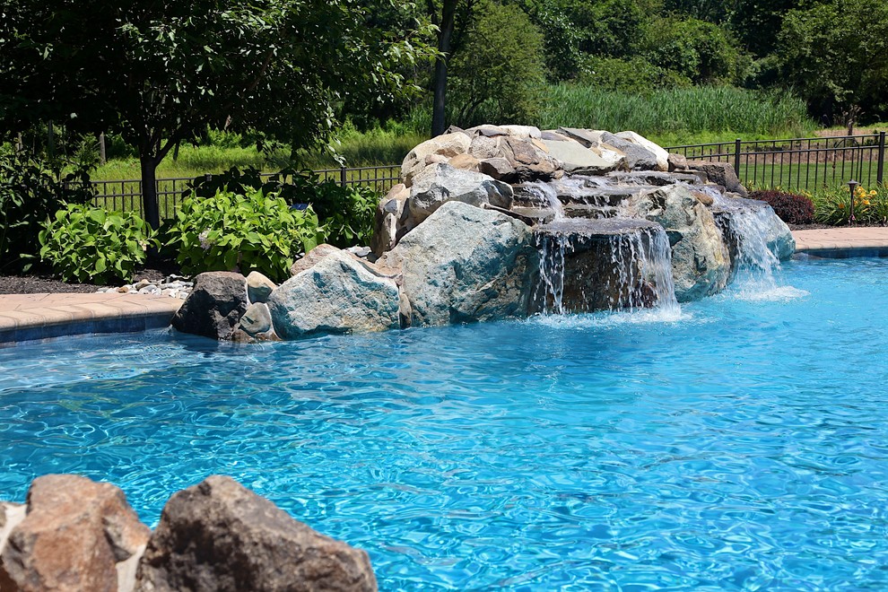 Design ideas for a mid-sized country backyard custom-shaped pool in New York with a water feature and brick pavers.