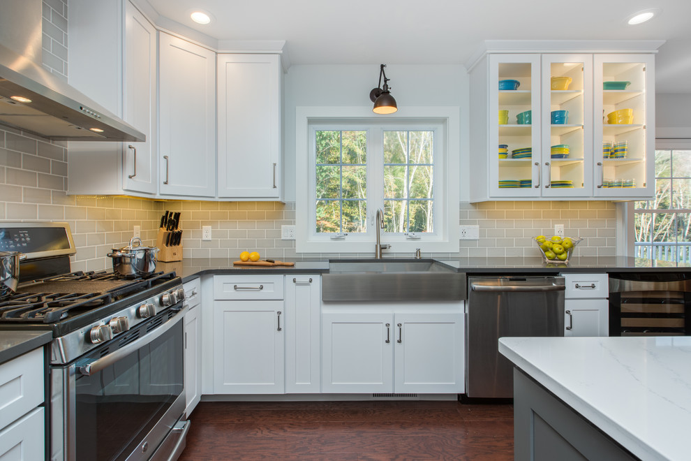 This is an example of a large transitional l-shaped open plan kitchen in Boston with a farmhouse sink, shaker cabinets, white cabinets, quartz benchtops, grey splashback, subway tile splashback, stainless steel appliances, with island and brown floor.