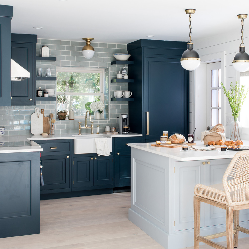 Beach style l-shaped eat-in kitchen in Minneapolis with a farmhouse sink, blue cabinets, quartz benchtops, grey splashback, subway tile splashback, stainless steel appliances, light hardwood floors, with island and white benchtop.