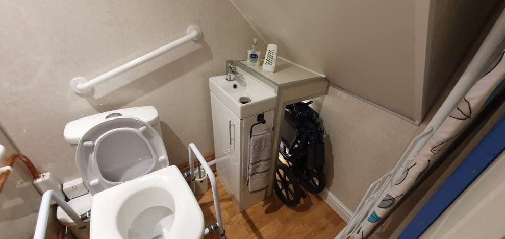 Bild på ett litet vintage grå grått toalett, med släta luckor, vita skåp, en toalettstol med hel cisternkåpa, grå kakel, grå väggar, vinylgolv, ett integrerad handfat, laminatbänkskiva och flerfärgat golv