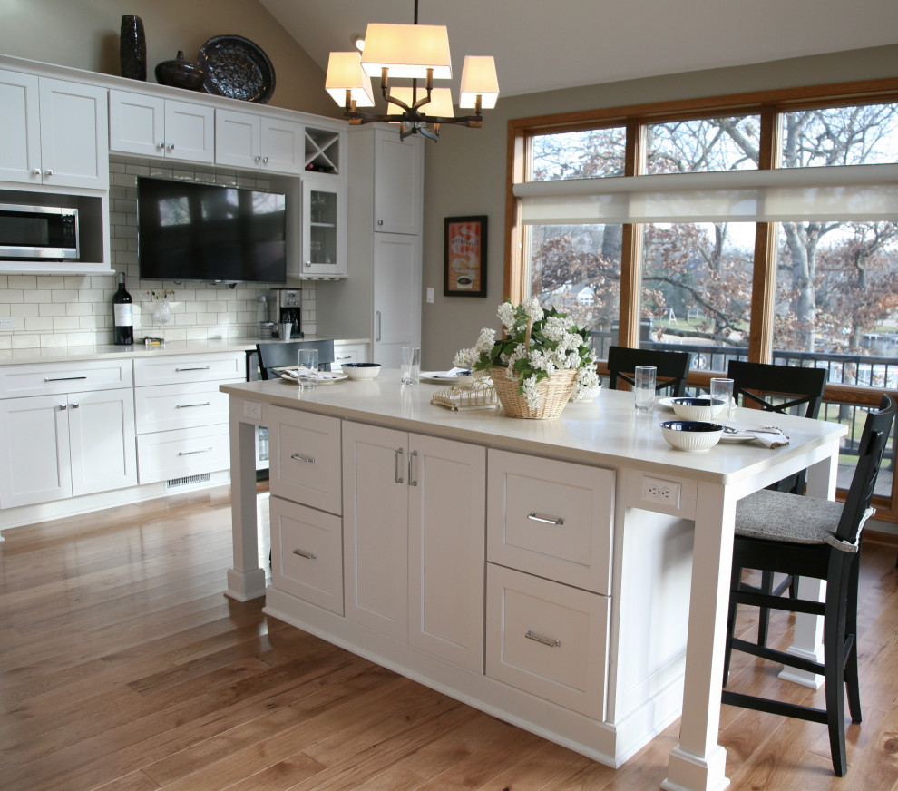 Large beach style kitchen/diner in Milwaukee with a submerged sink, shaker cabinets, white cabinets, engineered stone countertops, white splashback, porcelain splashback, stainless steel appliances, light hardwood flooring, multiple islands, brown floors, white worktops and a vaulted ceiling.
