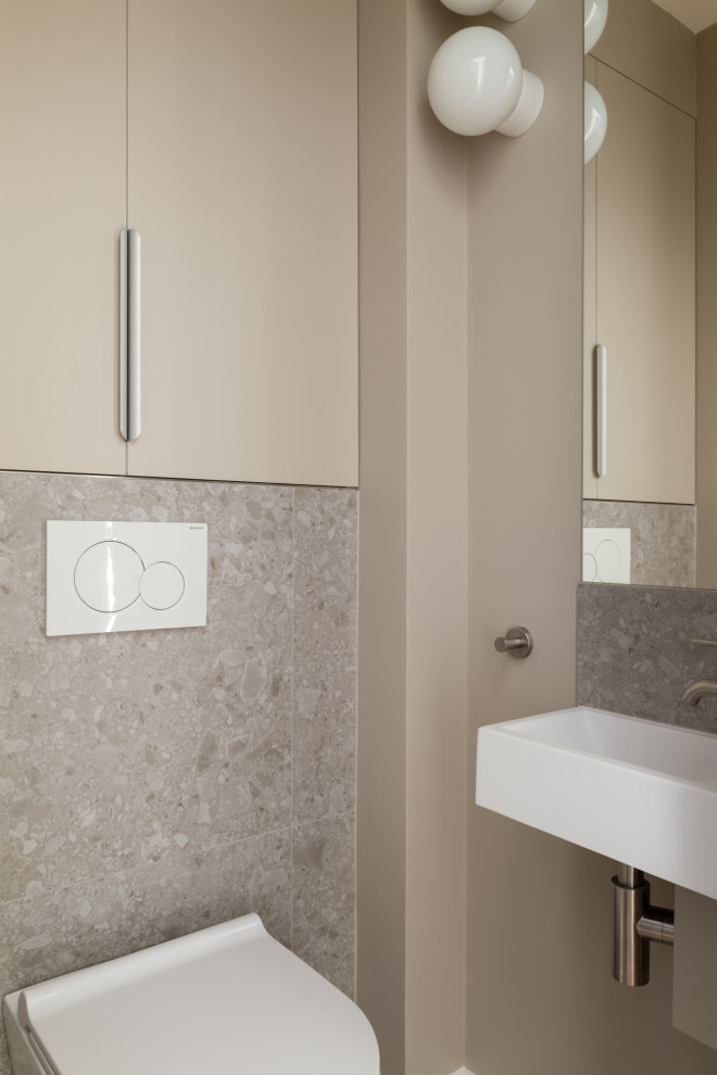 Modern inredning av ett litet toalett, med luckor med profilerade fronter, beige skåp, en vägghängd toalettstol, grå kakel, keramikplattor, beige väggar, klinkergolv i keramik, ett väggmonterat handfat och grått golv