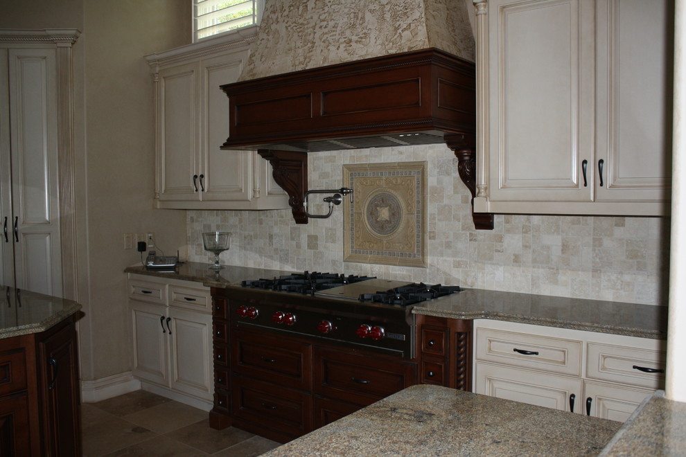 Large travertine floor kitchen photo with raised-panel cabinets, distressed cabinets, granite countertops, beige backsplash, stone tile backsplash, stainless steel appliances, brown walls and an island