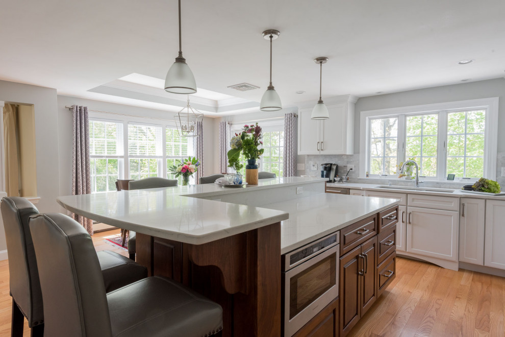 Inspiration for a large transitional l-shaped medium tone wood floor, brown floor and coffered ceiling eat-in kitchen remodel in Boston with an undermount sink, shaker cabinets, white cabinets, quartz countertops, gray backsplash, subway tile backsplash, stainless steel appliances, an island and white countertops