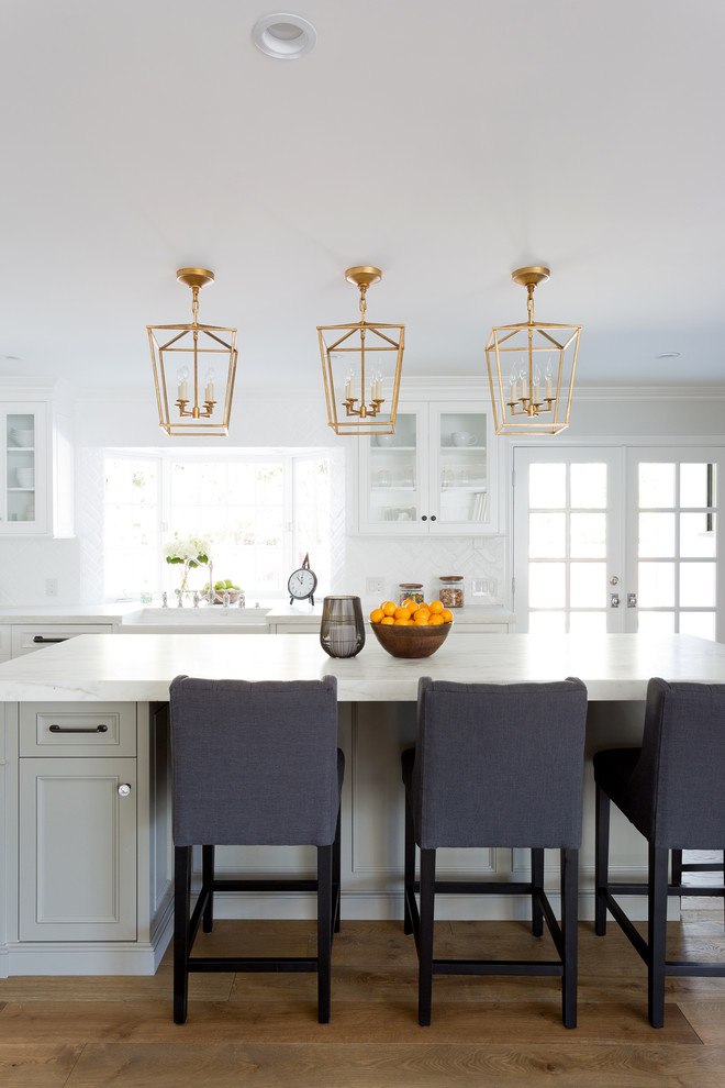 Open concept kitchen - large transitional l-shaped light wood floor open concept kitchen idea in Orange County with a farmhouse sink, shaker cabinets, white cabinets, marble countertops, white backsplash, brick backsplash, stainless steel appliances and an island