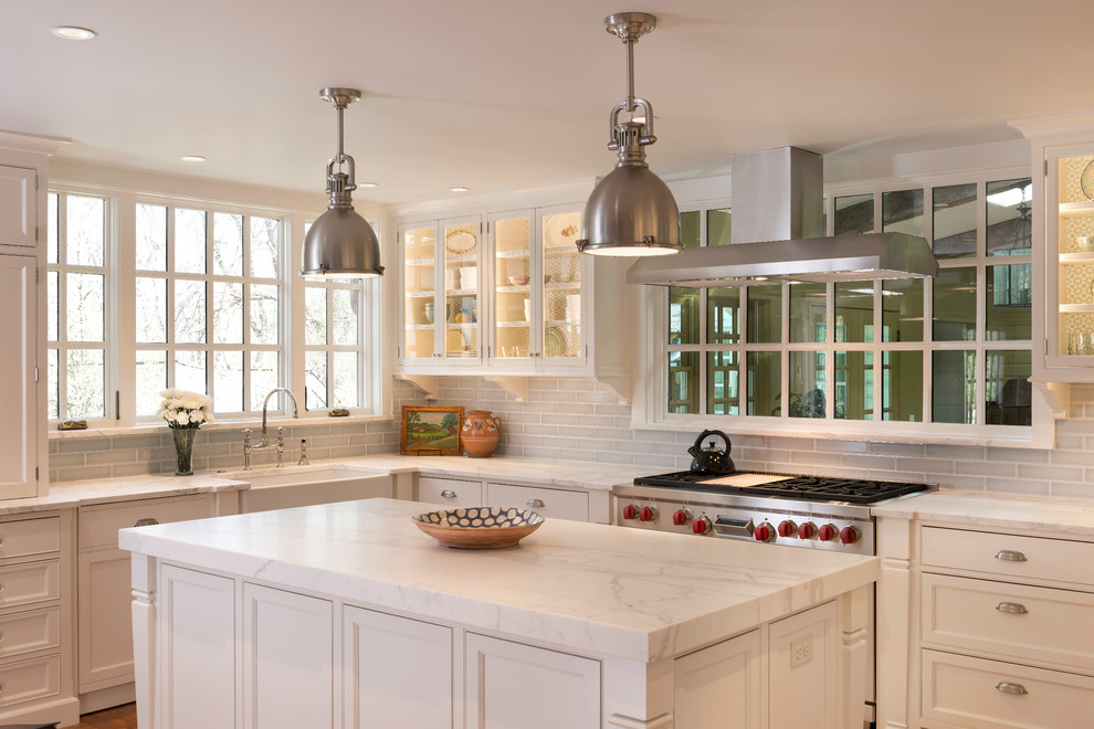 Design ideas for a country l-shaped kitchen in DC Metro with a farmhouse sink, white cabinets, marble benchtops, grey splashback, glass tile splashback, stainless steel appliances, medium hardwood floors, with island and glass-front cabinets.