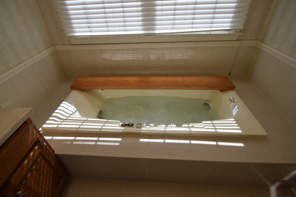 Example of a mid-sized transitional master beige tile and porcelain tile porcelain tile and gray floor drop-in bathtub design with raised-panel cabinets, medium tone wood cabinets, a one-piece toilet, blue walls, an undermount sink, marble countertops and multicolored countertops