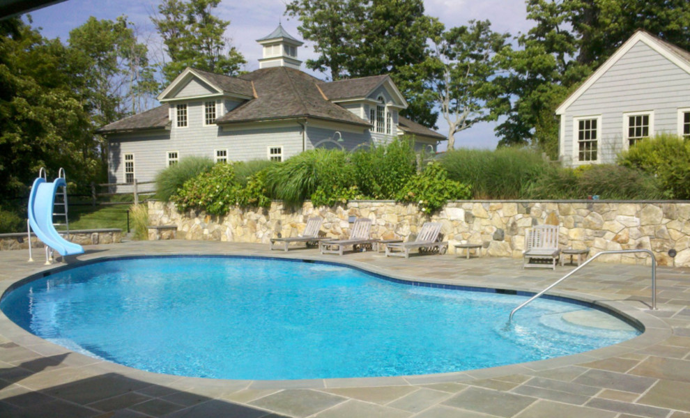 This is an example of a mid-sized traditional backyard kidney-shaped pool in New York with a water slide and tile.