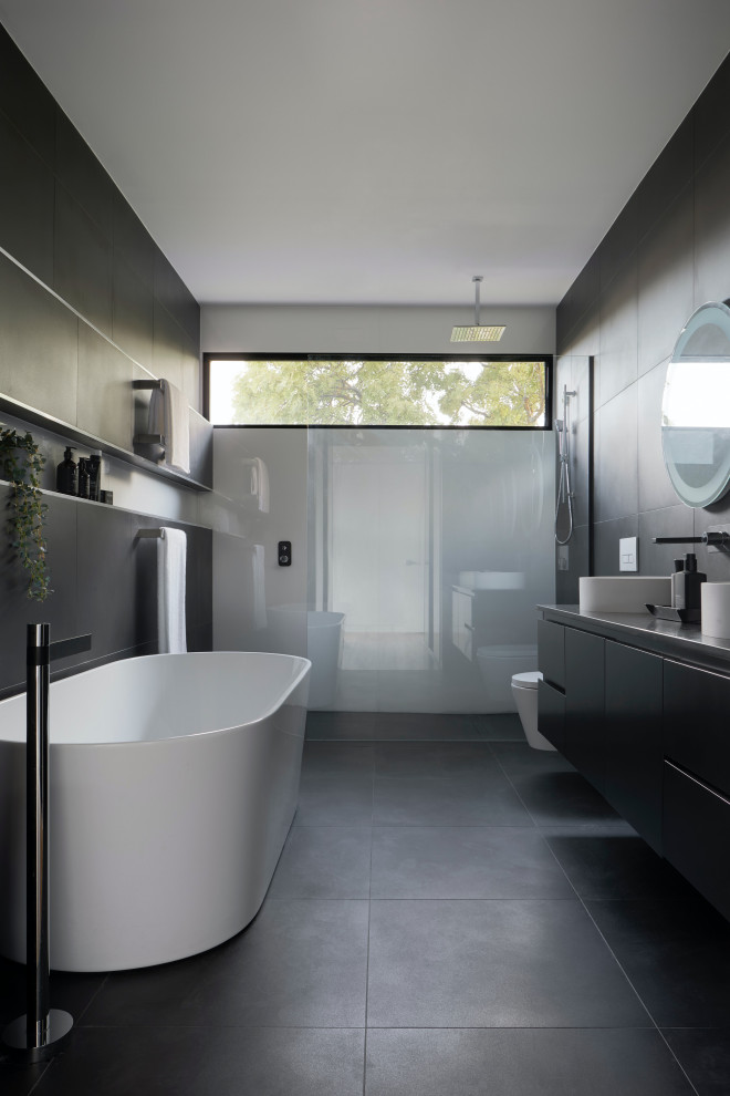 Mid-sized modern master bathroom in Sydney with recessed-panel cabinets, grey cabinets, a freestanding tub, an open shower, a wall-mount toilet, gray tile, ceramic tile, grey walls, ceramic floors, a trough sink, engineered quartz benchtops, grey floor, an open shower, grey benchtops, a niche, a double vanity, a floating vanity, recessed and panelled walls.