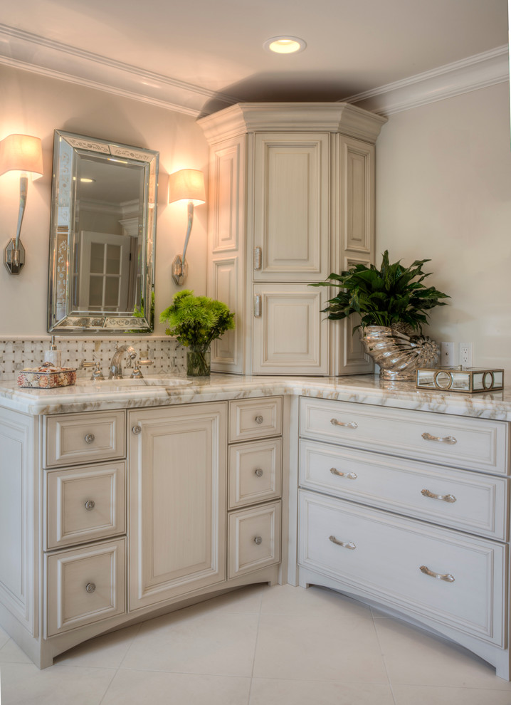 Photo of a large traditional bathroom in Other with an undermount sink, raised-panel cabinets, beige cabinets, marble benchtops, a freestanding tub, a one-piece toilet, beige tile, stone tile, beige walls and marble floors.