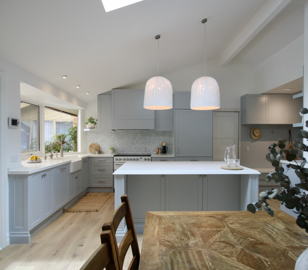 Design ideas for an expansive transitional open plan kitchen in Sydney with a farmhouse sink, shaker cabinets, grey cabinets, quartz benchtops, grey splashback, marble splashback, white appliances, medium hardwood floors, with island, brown floor and white benchtop.