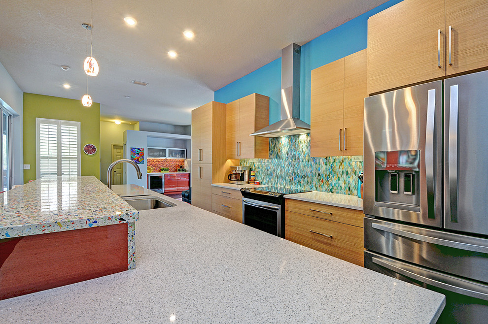 This is an example of a large contemporary galley open plan kitchen in Tampa with a single-bowl sink, flat-panel cabinets, light wood cabinets, recycled glass benchtops, blue splashback, glass tile splashback, stainless steel appliances, porcelain floors and with island.