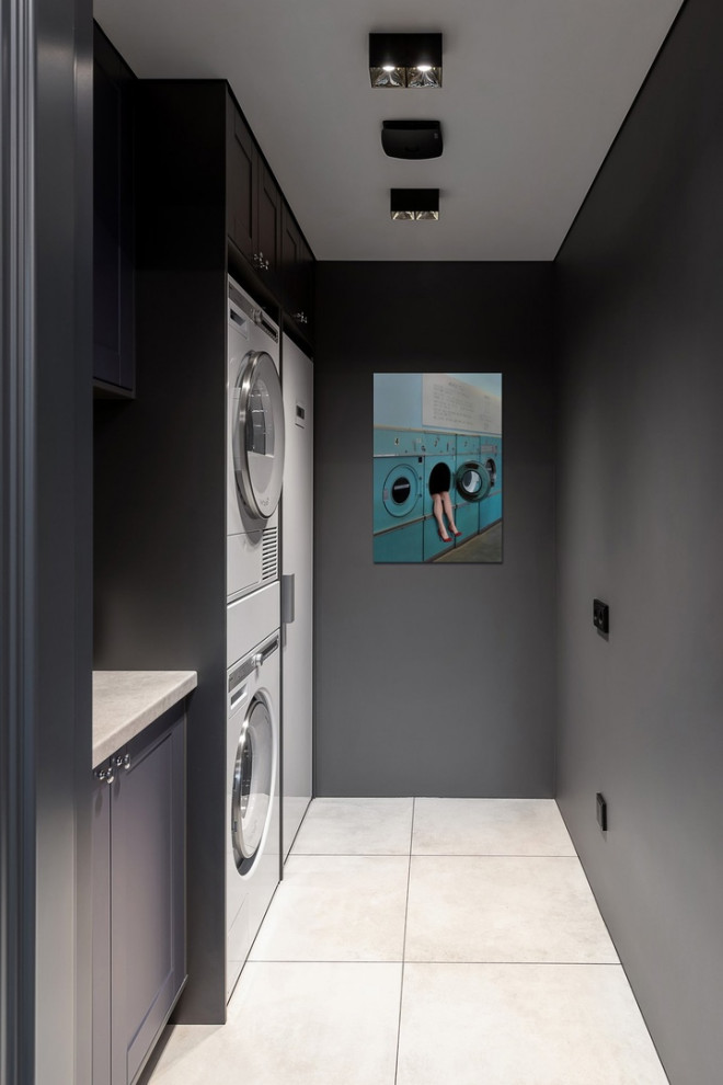 Large contemporary single-wall separated utility room in Other with ceramic flooring, white floors, panelled walls, a built-in sink, raised-panel cabinets, grey cabinets, laminate countertops, white splashback, ceramic splashback, grey walls, a stacked washer and dryer and white worktops.
