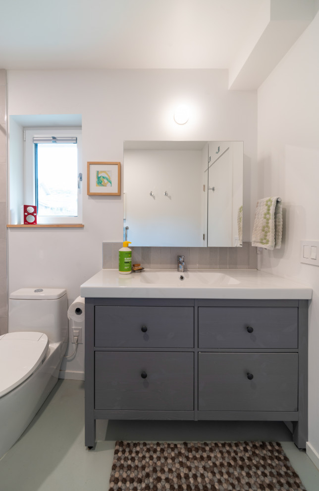 Design ideas for a modern bathroom in Vancouver with flat-panel cabinets, grey cabinets, an alcove bath, a one-piece toilet, white tiles, porcelain tiles, white walls, concrete flooring, an integrated sink, laminate worktops, a shower curtain, white worktops, a single sink and a freestanding vanity unit.