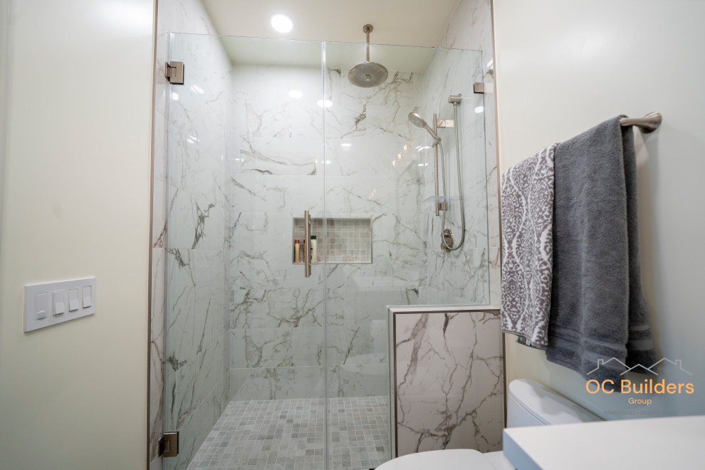 Foto på ett litet vintage vit badrum med dusch, med vita skåp, en dusch i en alkov, en toalettstol med hel cisternkåpa, flerfärgad kakel, porslinskakel, vita väggar, ett nedsänkt handfat, laminatbänkskiva, dusch med gångjärnsdörr, luckor med infälld panel och grått golv