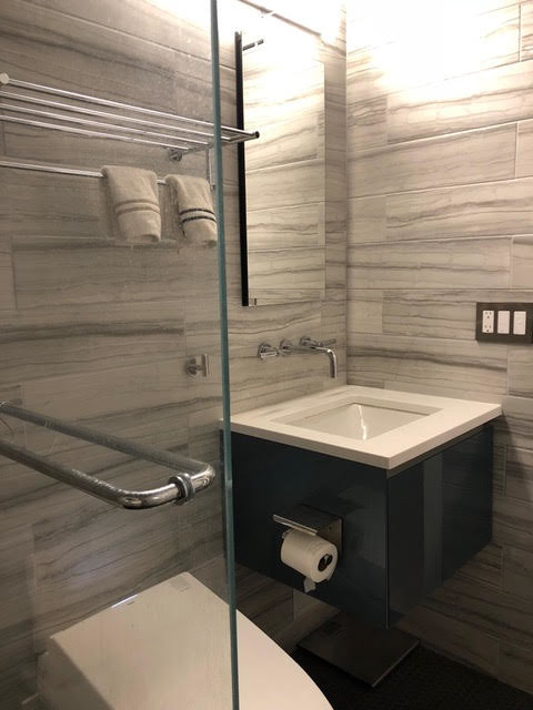 Small contemporary 3/4 bathroom in New York with flat-panel cabinets, black cabinets, an alcove shower, a one-piece toilet, gray tile, marble, grey walls, porcelain floors, an undermount sink, solid surface benchtops, black floor, a hinged shower door and white benchtops.